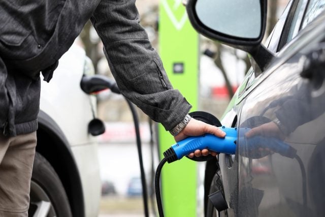 Male hand holding electrical socket while charging electrocar