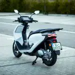 Elektrická mobilita už dávno nie je výsadou automobilov. Čoraz výraznejšie preniká aj medzi jednostopové vozidlá a Honda patrí medzi výrobcov, ktorí tento trend berú mimoriadne vážne. Model CUV e: je dôkazom, že elektrický skúter nemusí byť technologickou kuriozitou, ale môže predstavovať praktický dopravný prostriedok pre každodenný život v meste. Treba si však hneď na úvod uvedomiť jednu vec. Honda CUV e: nie je motorka, ktorá bude vodiča odmeňovať adrenalínovými zážitkami alebo športovým charakterom. Jej poslanie je úplne iné. Má byť tichým, spoľahlivým a nenáročným partnerom pri každodenných presunoch z domu do práce, na nákup či za povinnosťami. Nestarne po prvom pohľade Honda pri modeli CUV e: nešla cestou extravagantných tvarov ani nostalgických retro prvkov. Dizajn pôsobí čisto, moderne a funkčne. Predná časť je elegantne tvarovaná, kompaktné proporcie uľahčujú pohyb v hustej premávke a človek počas každodenného používania ocení aj plochú podlahu. Nastupovanie je jednoduchšie, rovnako ako prevážanie tašky, batohu či menšieho nákupu. Elektrický pohon pre mestské tempo O pohon sa stará elektromotor s maximálnym výkonom 6 kW a krútiacim momentom 22 Nm. Parametre zodpovedajú približne klasickému skútru s objemom 125 cm³, pričom maximálna rýchlosť približne 83 km/h úplne postačuje na mestskú premávku aj kratšie presuny po obchvate alebo prímestských komunikáciách. Najväčší rozdiel oproti spaľovaciemu skútru však, pochopiteľne, spočíva v spôsobe, akým výkon odovzdáva. Elektrický pohon reaguje okamžite. Bez radenia, bez oneskorenia variátora a bez akýchkoľvek vibrácií. Rozjazdy zo semaforov sú plynulé a tiché, pričom jazdec si veľmi rýchlo zvykne na okamžité reakcie. V hustej premávke dokáže CUV e: pôsobiť prekvapivo svižne. Vyberateľné batérie ako najväčšia výhoda Jedným z najzaujímavejších riešení modelu CUV e: je použitie dvojice vyberateľných lítiovo-iónových batérií Honda Mobile Power Pack e:. Každá disponuje kapacitou 1,3 kWh, spolu teda ponúkajú 2,6 kWh využiteľnej energie. Jedna batéria váži približne 10,2 kilogramu, takže ich síce možno prenášať, no nedá sa hovoriť o riešení bez námahy. Ich výhodou je možnosť nabíjania mimo samotného skútra. To ocenia najmä ľudia bývajúci v bytových domoch alebo všade tam, kde nie je možné zaparkovať skúter priamo pri elektrickej zásuvke. Na druhej strane treba počítať s tým, že každú batériu je potrebné nabíjať samostatne. Úplné nabitie jednej trvá približne šesť hodín. Honda udáva dojazd okolo 70 kilometrov, pričom v praxi bude závisieť predovšetkým od štýlu jazdy, teploty aj profilu trasy. Pre bežné mestské dochádzanie ide o hodnotu, ktorá väčšine používateľov postačí. Ak však niekto plánuje počas dňa absolvovať desiatky kilometrov naprieč mestom, bude musieť hospodárenie s energiou predsa len viac plánovať. Výška sedla približne 760 milimetrov, hmotnosť okolo 120 kilogramov a nízko uložené ťažisko robia zo skútra veľmi prístupný dopravný prostriedok aj pre menej skúsených jazdcov. V hustej premávke pôsobí ľahko, prirodzene mení smer a neunavuje vodiča ani počas dlhšieho jazdenia. Parkovanie či manipulácia v stiesnených priestoroch sú mimoriadne jednoduché. Praktickým detailom je systém Reverse Assist. Ide o pomalý elektrický spätný chod s rýchlosťou približne 3 km/h. Limity praktickosti Výbava zodpovedá dnešným očakávaniam od moderného mestského skútra. Honda ponúka 7-palcový TFT displej, konektivitu Honda RoadSync Duo, bezkľúčové ovládanie Smart Key, LED osvetlenie aj USB konektor na nabíjanie mobilných zariadení. Určitým kompromisom je však batožinový priestor. Keďže pod sedadlom sú umiestnené obe batérie, klasický úložný priestor prakticky neexistuje. Nepodarí sa sem uložiť ani prilbu či menší nákup, čo znamená, že sa musíte spoľahnúť buď na batoh alebo nejaké doplnkové príslušenstvo, napríklad horný kufor. Otáznik vyvoláva aj brzdová sústava. Honda použila kombinovaný brzdový systém CBS, ktorý rozdeľuje brzdnú silu medzi obe kolesá. V tejto kategórii by však prítomnosť systému ABS pôsobila istejšie, najmä pri jazde na mokrej vozovke alebo po dlažobných kockách, kde môže byť jeho prínos výrazný. Verdikt Najväčšími prednosťami sú kultivovaný elektrický pohon, jednoduché ovládanie, možnosť vyberania batérií a veľmi príjemná manévrovateľnosť. Na druhej strane treba počítať s obmedzeným úložným priestorom pod sedadlom a absenciou systému ABS. Ak však prijmete filozofiu tohto skútra a nebudete od neho očakávať emócie veľkej motorky, Honda CUV e: začne veľmi rýchlo dávať zmysel. Je tichá, nenáročná, praktická a presne zapadá do rytmu mesta, kde rozhodujú každodenná použiteľnosť, nízke prevádzkové náklady a jednoduchosť. Práve v tomto prostredí ukazuje, že môže byť jedným z najpraktickejších spôsobov mestskej mobility. Kolesami nadol, priatelia. NÁZOV: Honda CUV e: MOTOR: elektrický, max. 6 kW HMOTNOSŤ: cca 119 kg VÝŠKA SEDLA: 760 mm CENA: 4 590 €